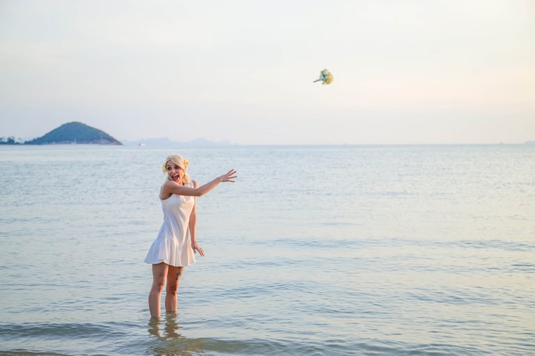 Bride tossing bouquet in shallow sea at sunset