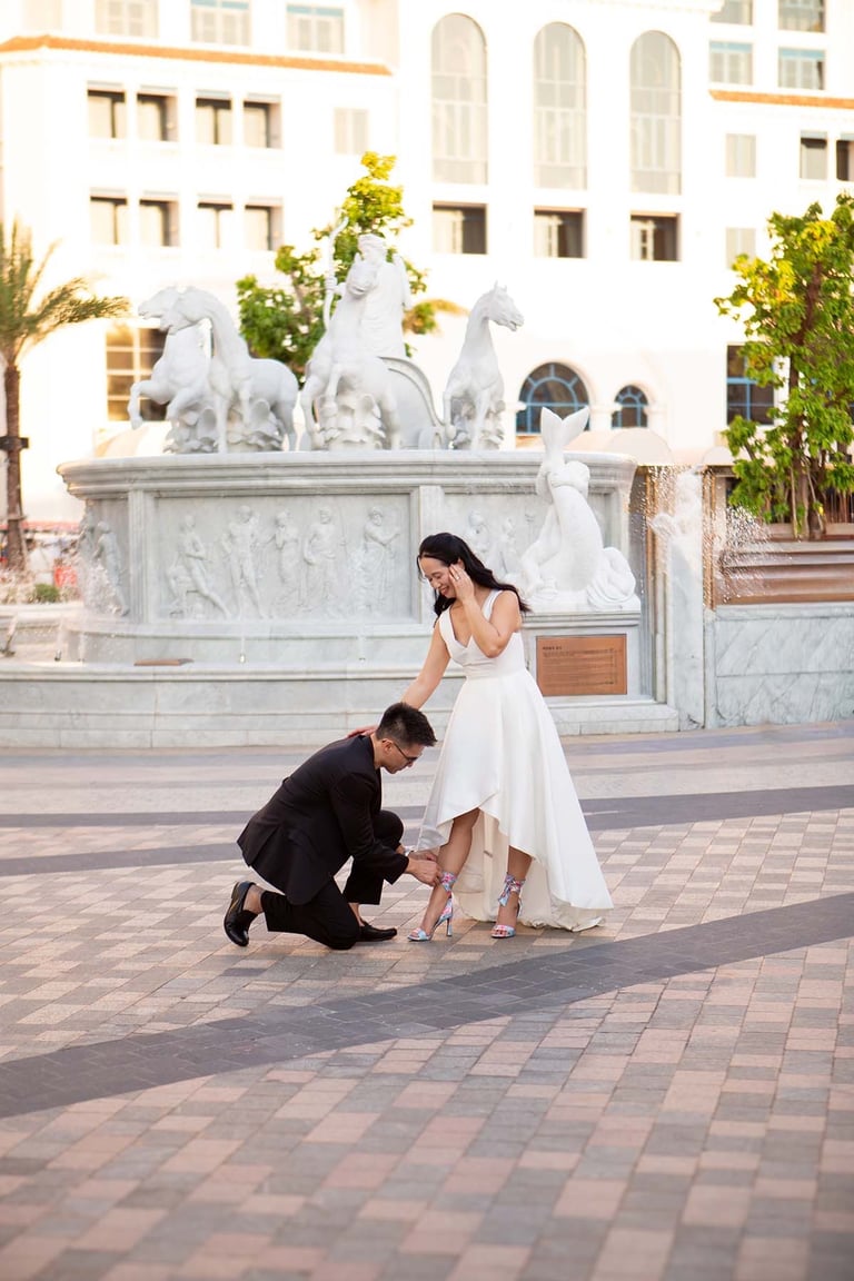 Groom fixing bride heels near fountain in Sunset Town