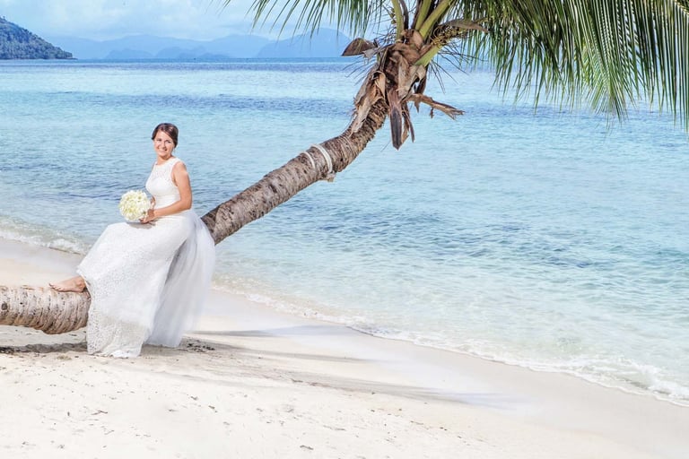 Bride sitting on palm trunk by turquoise sea
