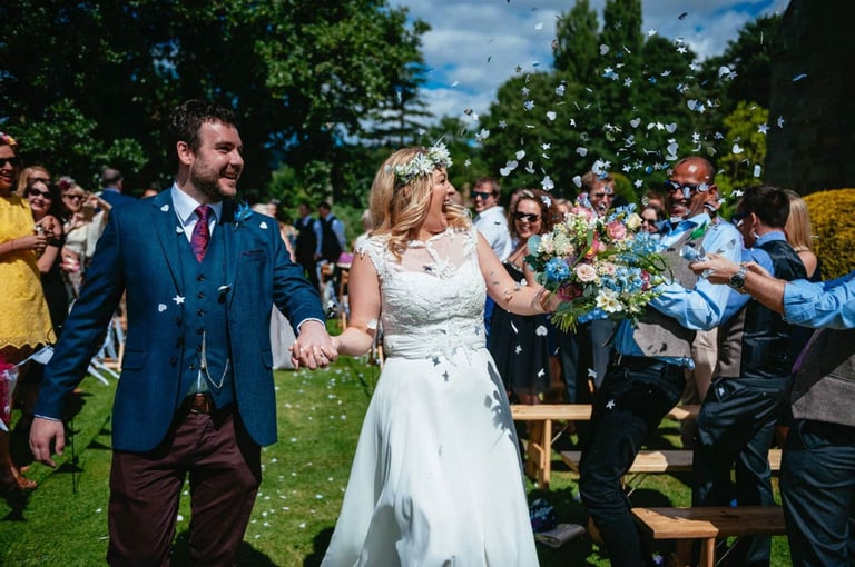 Confetti joy as the couple walk hand in hand at Brinsop Court Manor House and Barn, surrounded by smiling guests.