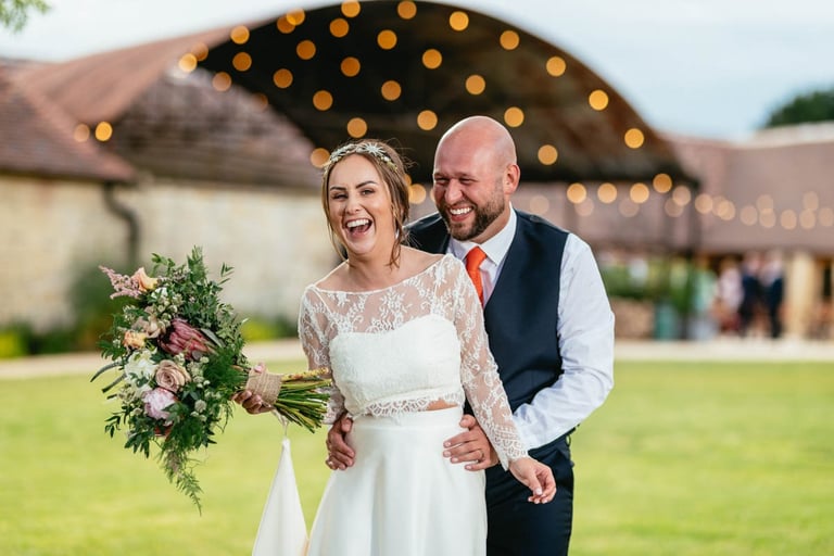 Bride and groom laughing outside Old Gore barn wedding venue in the Cotswolds, captured candidly by photographer Owen Mathias