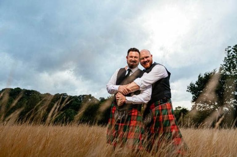 Groom and groom in kilts embrace in a golden field at Ceridwen Centre wedding, South Wales photography