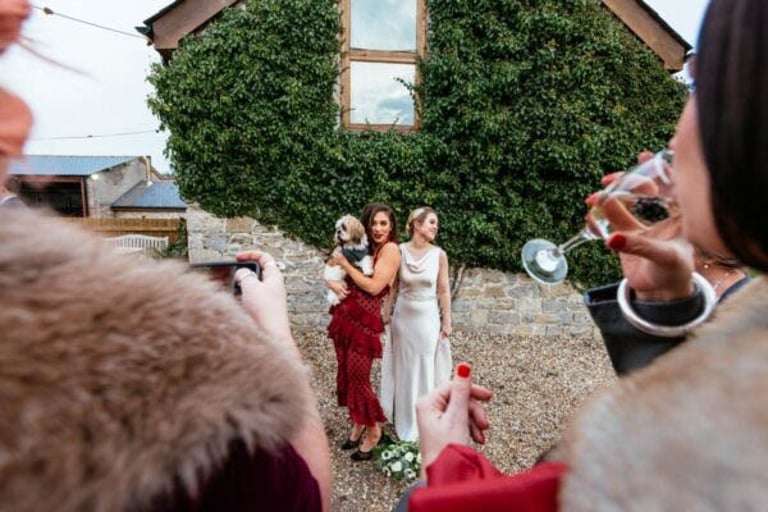 Wedding guests photographing brides outside ivy-covered barn at Rosedew Farm, South Wales, captured by Owen Mathias