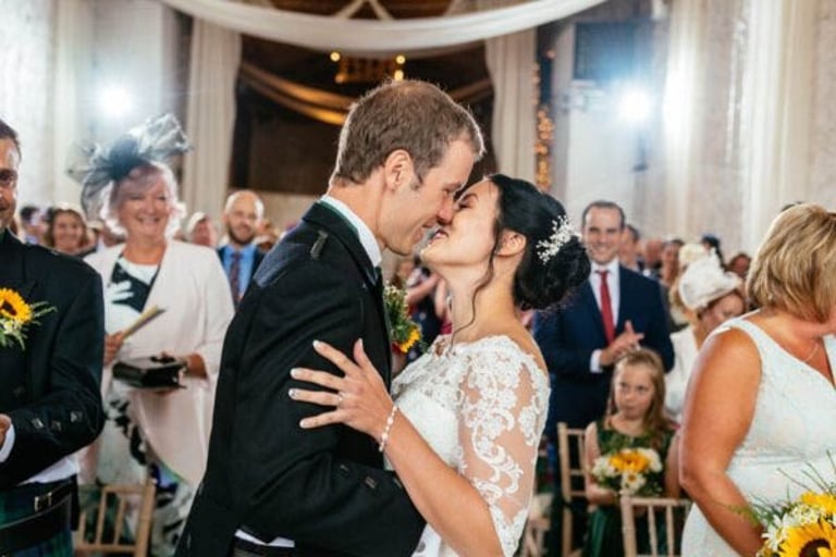 Newlyweds share a joyful kiss at Rosedew Farm, surrounded by smiling guests and summer florals in the ceremony.