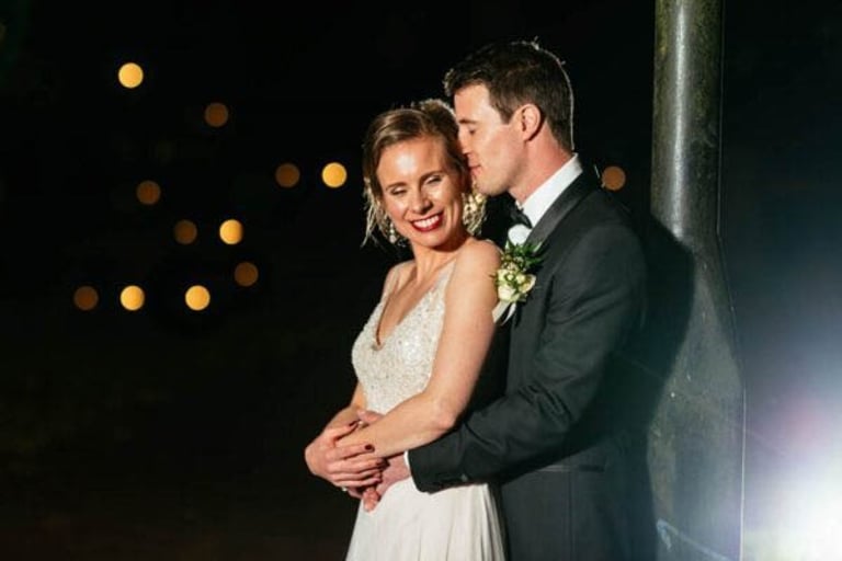 Bride and groom embrace under warm night lights, captured with a romantic glow and soft laughter.
