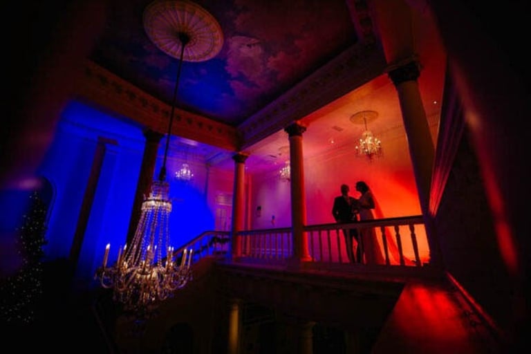 Angel Hotel Cardiff wedding photography, couple silhouetted on balcony under chandeliers and vibrant lighting.