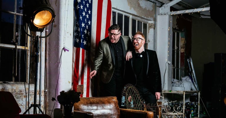 Fun gay wedding photography in London, grooms laughing together with bold urban backdrop and US flag