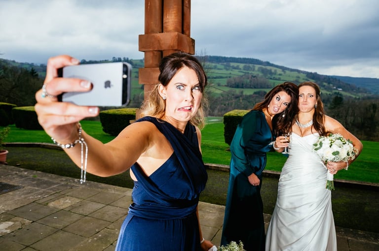 Bridesmaid taking funny selfie with bride and guest at South Wales wedding, captured candidly by photographer Owen Mathias