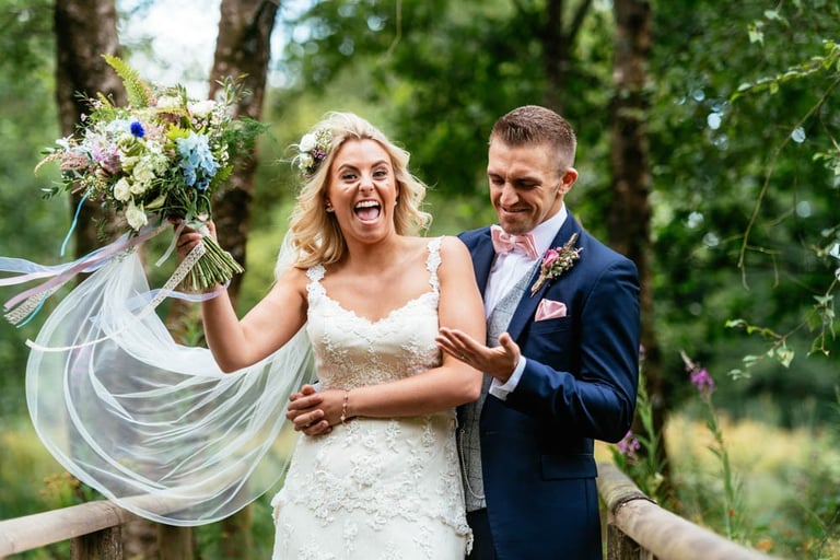 Bride and groom laughing on wooden bridge at Llanerch Vineyard wedding in South Wales, captured candidly by Owen Mathias