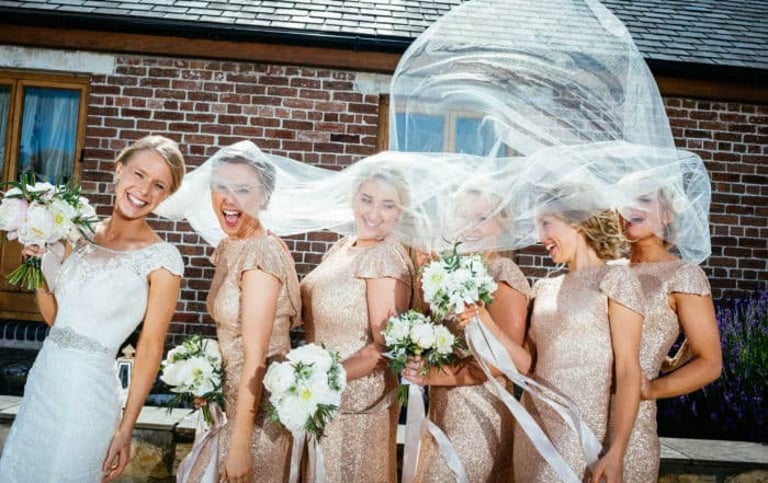 Bridal party laughing as wind lifts the bride’s veil at Rosedew Farm wedding, fun South Wales photography