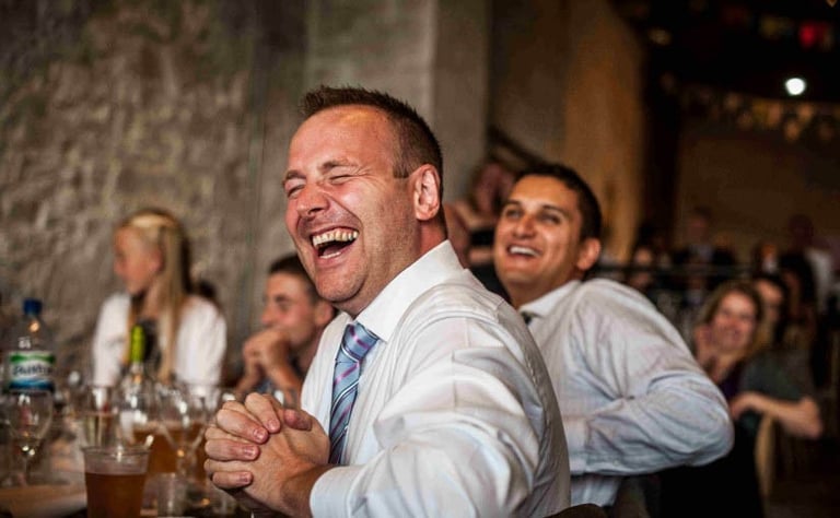 Wedding guest laughs during speeches at South Wales reception, captured in natural candid style by photographer Owen Mathias