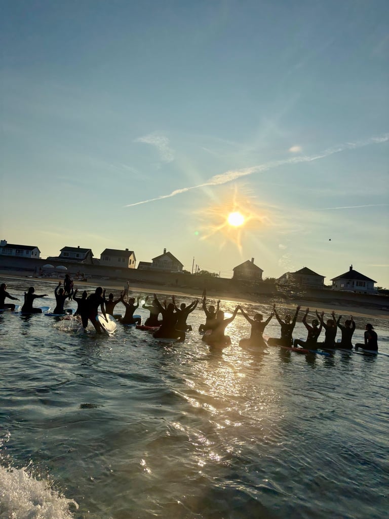 Surfers on boards holding hands in a memorial paddle out ceremony at sunset in the ocean.
