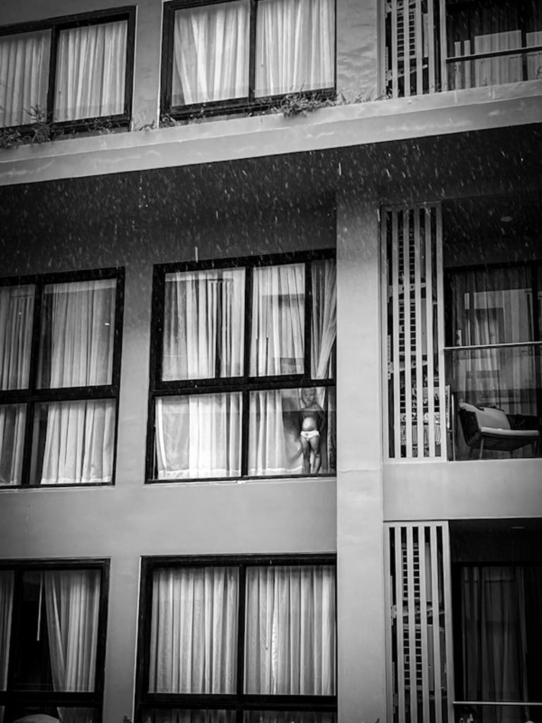 Baby watching the rain through the hotel window