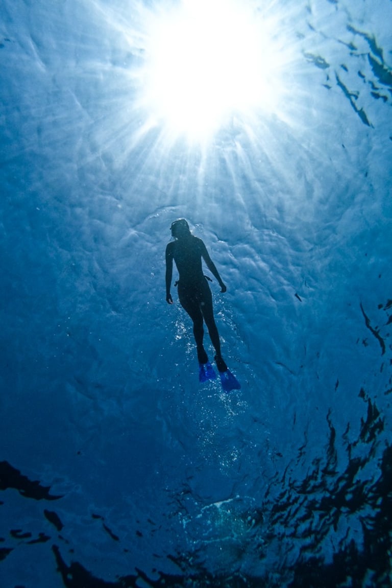 Silhouette of a woman at the sea surface with sunlight backlighting.