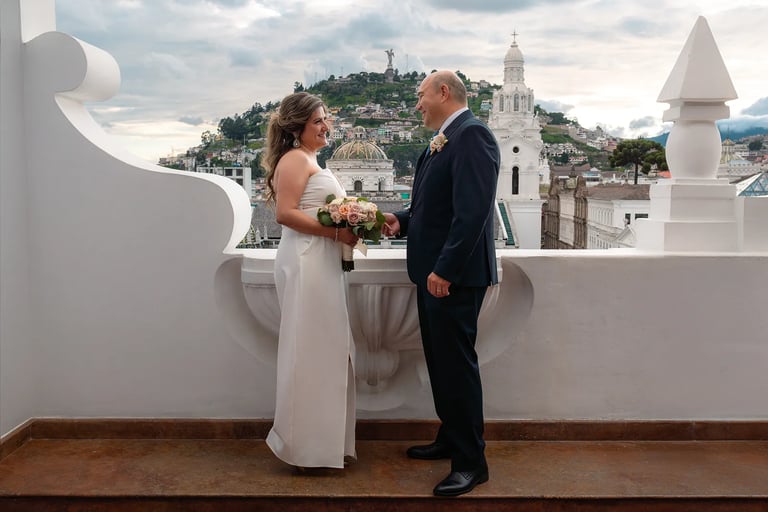 Una pareja de novios recién casada posando con el Panecillo de fondo viéndose con amor
