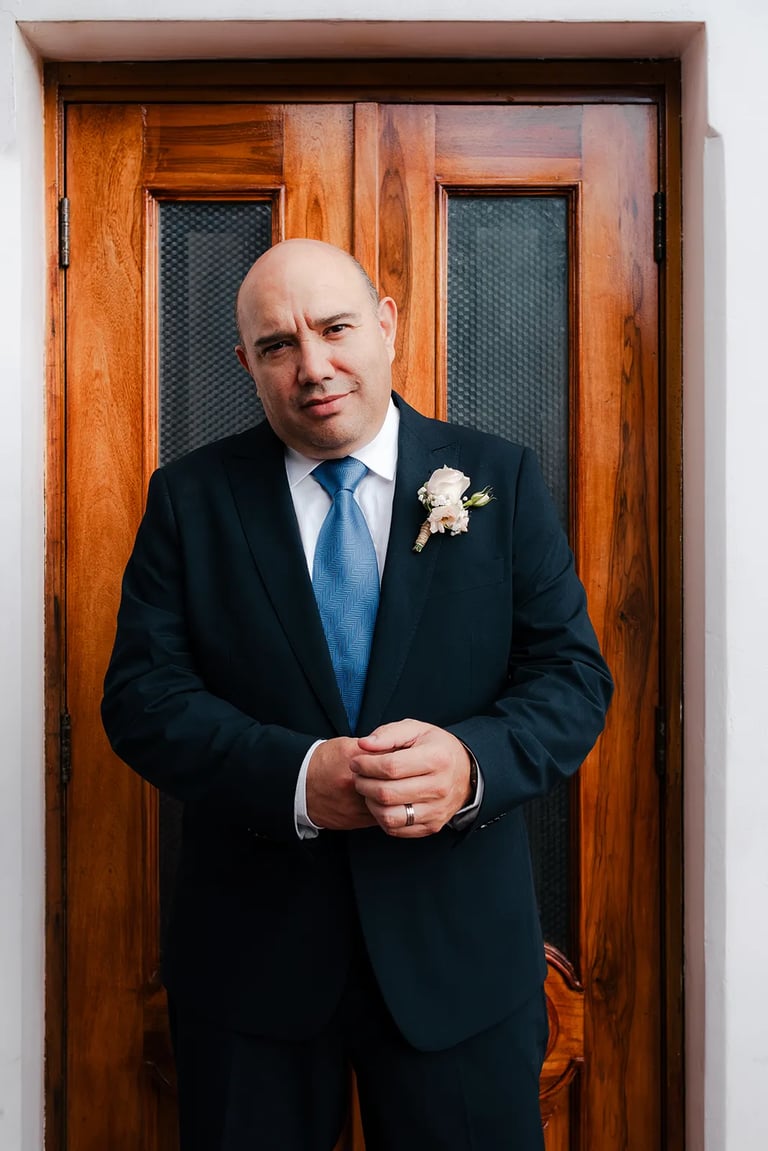 Novio en el día de su boda vestido con un traje elegante en una puerta de un salón de eventos en el centro histórico de Quito