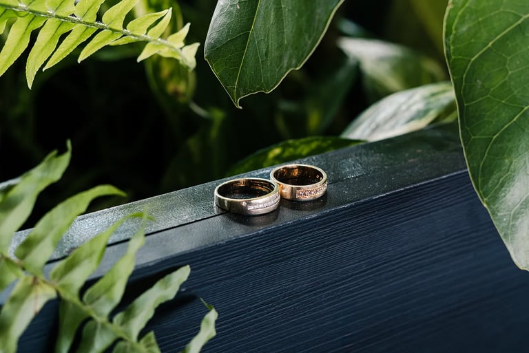 Fotografía premium de detalle de anillos de bodas reodeados de plantas en un fondo de madera azul en Quito