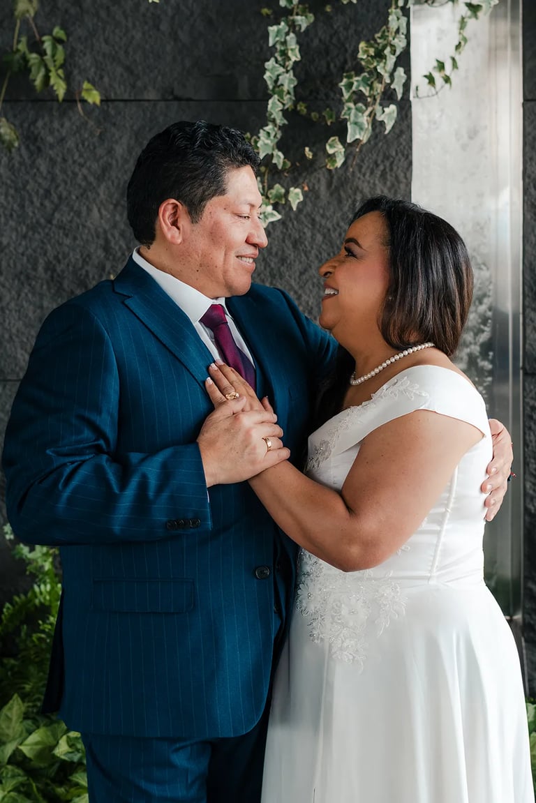 Retrato editorial de novios sonriendo en locación elegante con plantas en Quito. Fotografía documental de bodas premium.