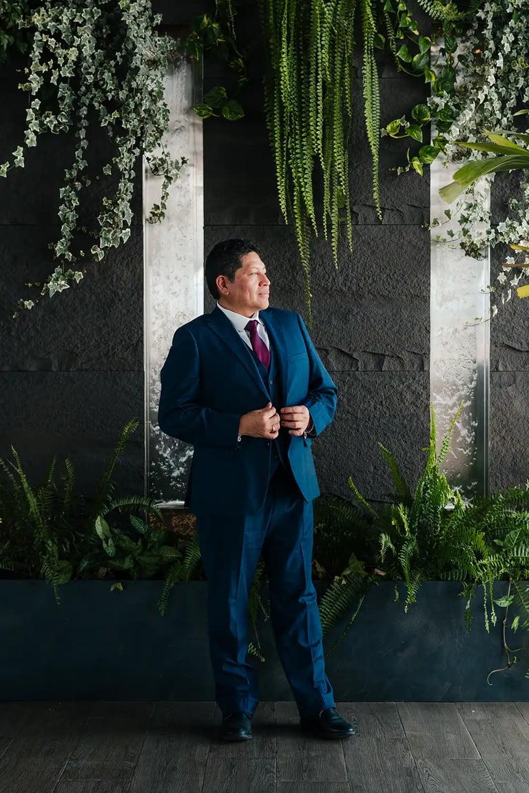 Retrato editorial de novio en locación elegante con plantas en Quito. Fotografía documental de bodas premium.