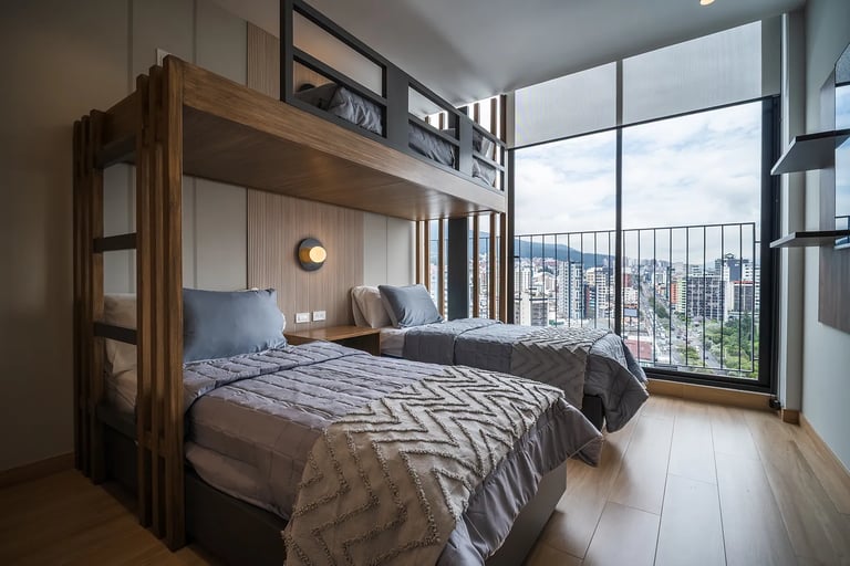 Tres camas una litera en una habitación con ventanal con vista hacia la ciudad de un airbnb en quito