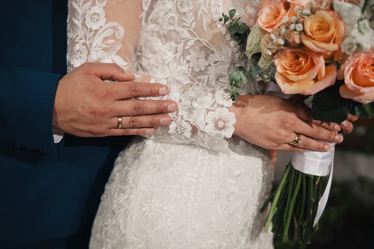 Detalle de manos de recien casados mostrando su anillo con ramo de flores en boda de Quito