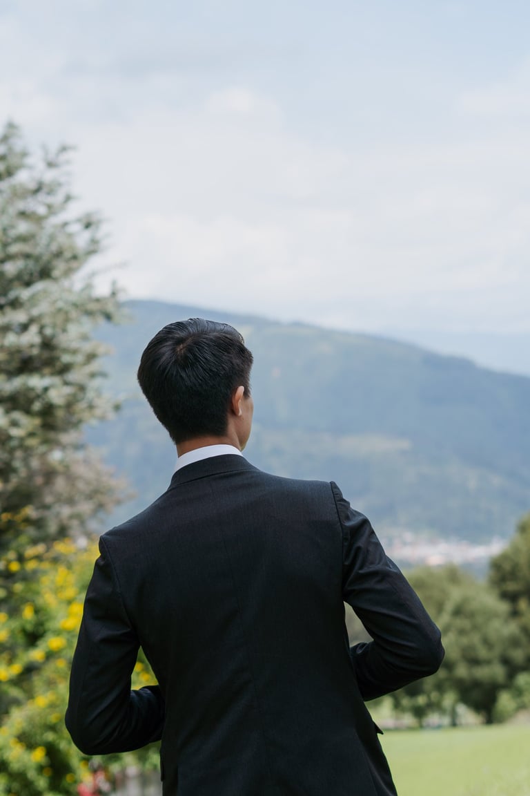 Hombre delgado con un traje negro elegante y bien peinado viendo de espaldas a la montaña
