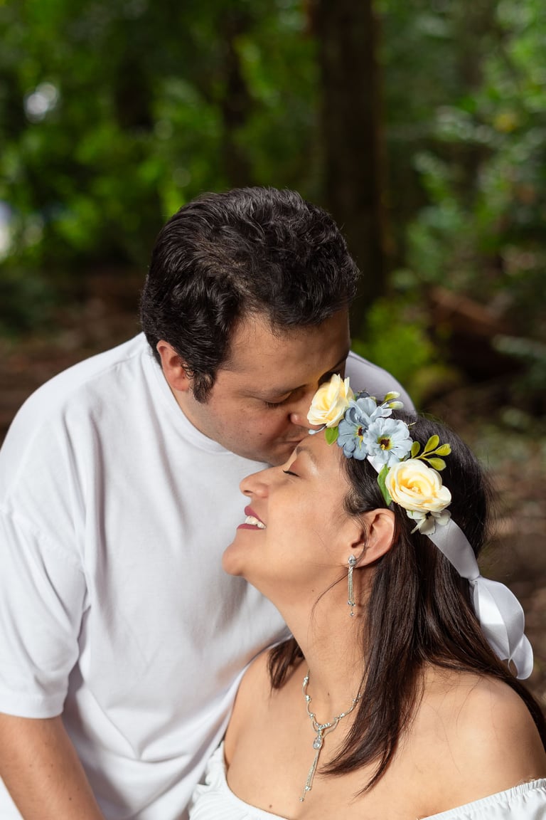 Fotografía profesional de maternidad con dos esposos que se aman vestidos de blanco en un bosque