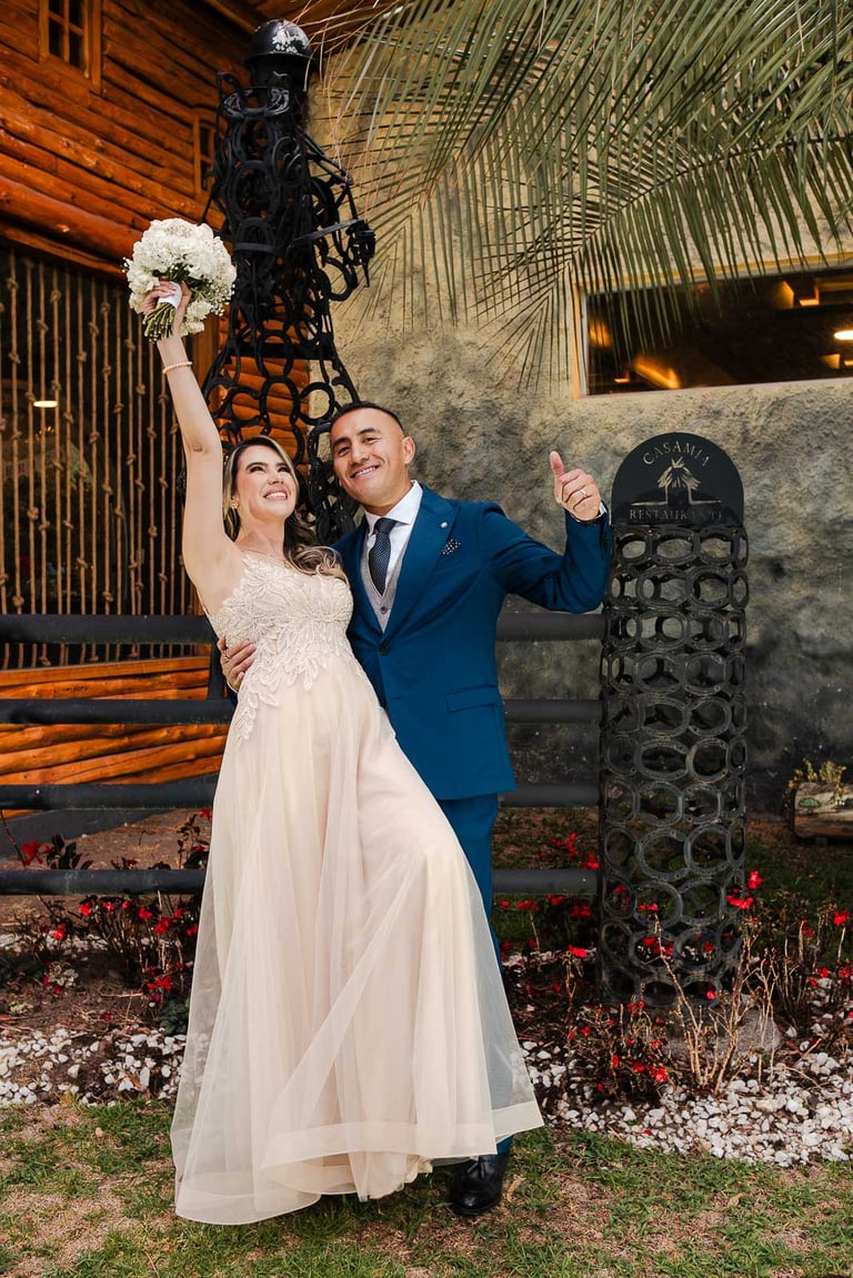Recién casados celebrando sonriendo a cámara. La novia levanta el ramo y disfrutan de su momento juntos en Quito, Ecuador