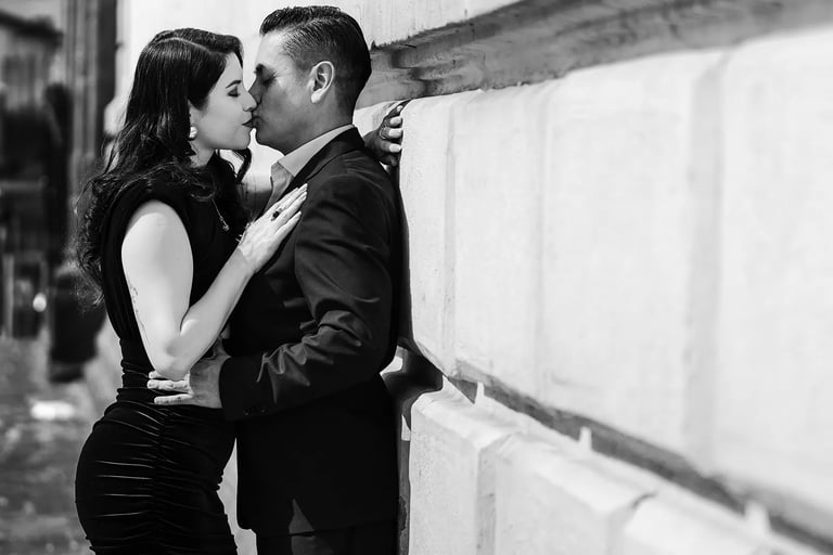 Plano medio de comprometidos dándose un beso amoroso en una pared en blanco y negro