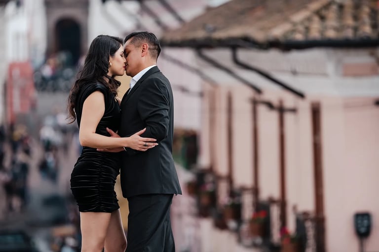 Pareja de novios dándose un beso apasionado y con amor con el fondo del centro histórico muy desenfocado