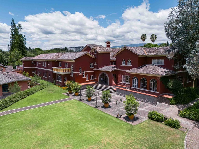 Fotografía aérea de gran casa religiosa de color rojo rodeada de hermoso jardín verde en Quito Ecuador