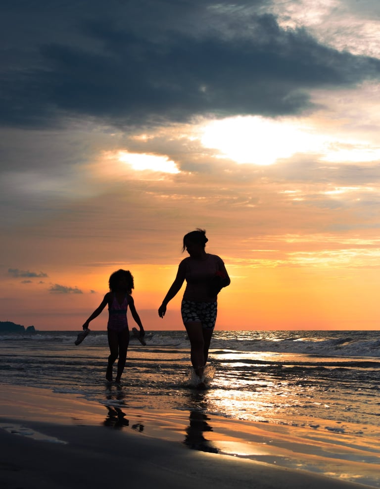 Retrato de una madre y su hija caminando por el agua de la playa en un atardecer