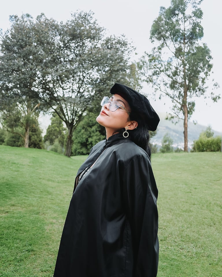 Mujer blanca con lentes feliz viendo al cielo con su uniforme de graduada en medio del césped