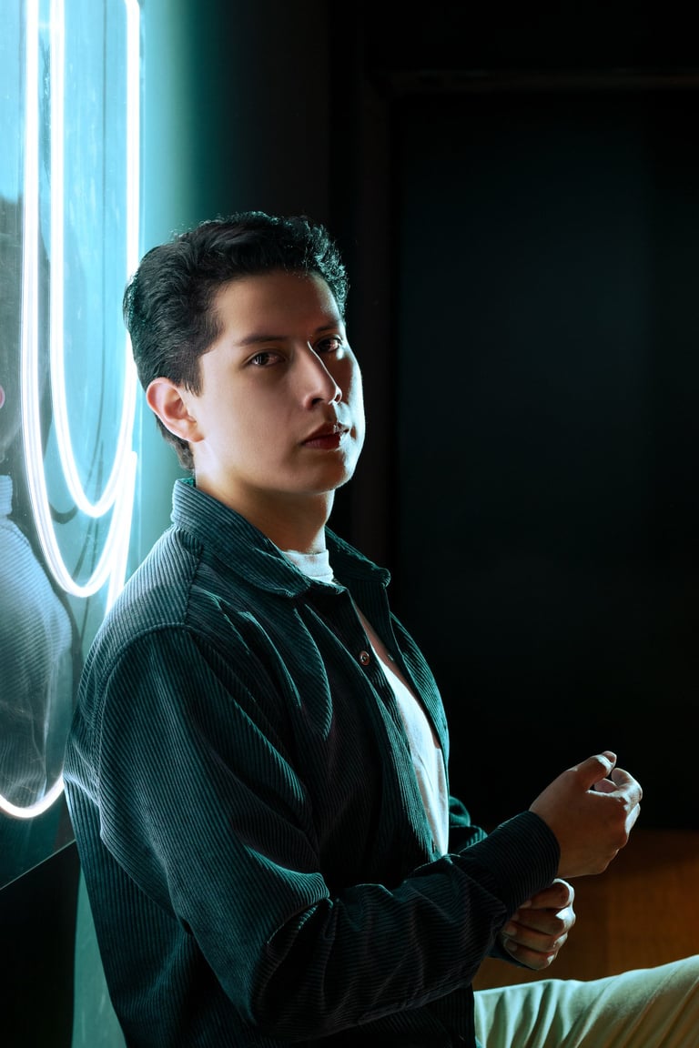 Hombre joven y apuesto sentado frente a luces de neon color azul con camisa de tela 