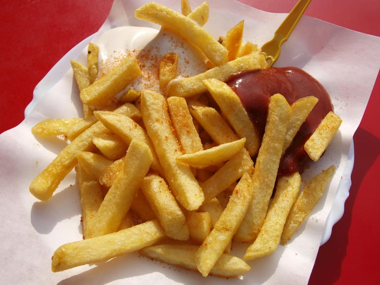 Crispy golden French fries served with ketchup and mayonnaise on a paper plate.
