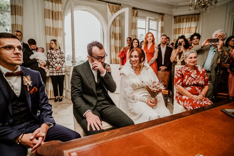 Cérémonie de mariage dans une salle élégante, avec le marié ému essuyant une larme, la mariée souriante en robe blanche avec 
