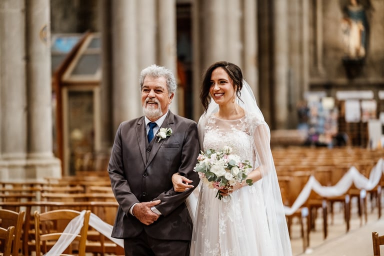 Mariée souriante entrant dans l’église au bras de son père, portant une robe blanche et un bouquet de fleurs, cérémonie de ma