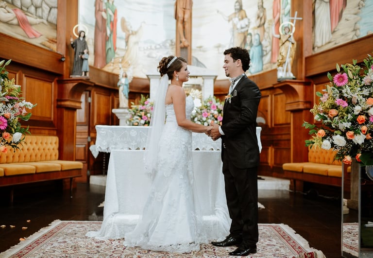 Photo de mariage dans une église : la mariée en robe blanche et le marié en costume noir se tiennent la main devant l'autel d