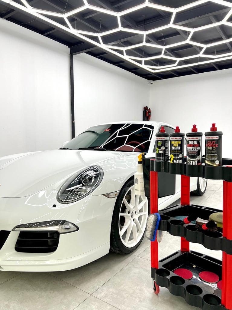 White luxury sports car in a detailing shop with professional polishing compounds on a tool cart.