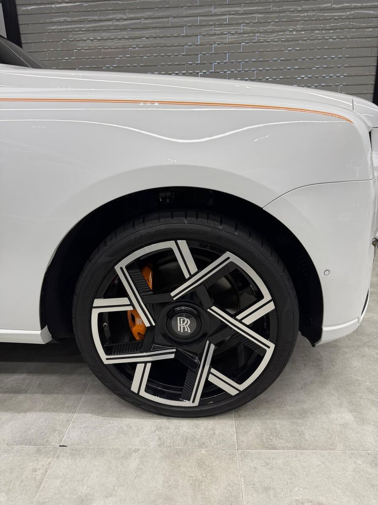Close-up of a white Rolls-Royce luxury car wheel with custom black and silver rims and orange brake calipers.