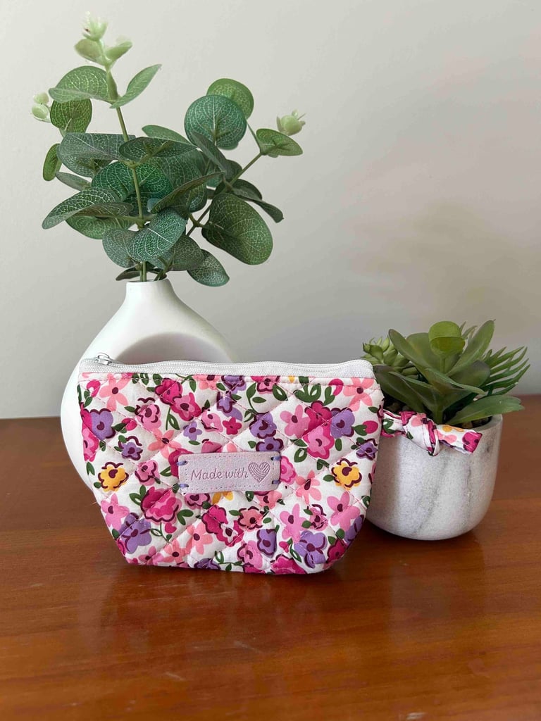 Une pochette matelassée à motif floral rose, confectionnée à la main, posée sur une table en bois.