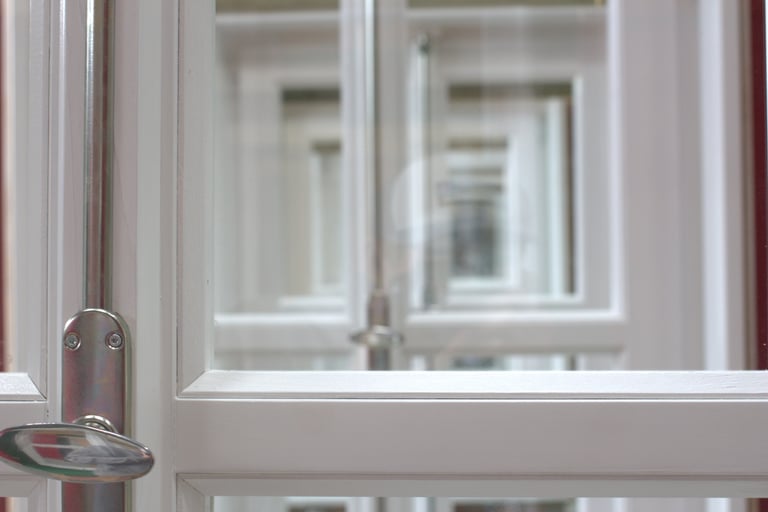 Detailaufnahme eines weiß lackierten Holzrahmen-Glas­fensters mit Metallgriff, Blick durch mehrere Fensterrahmen