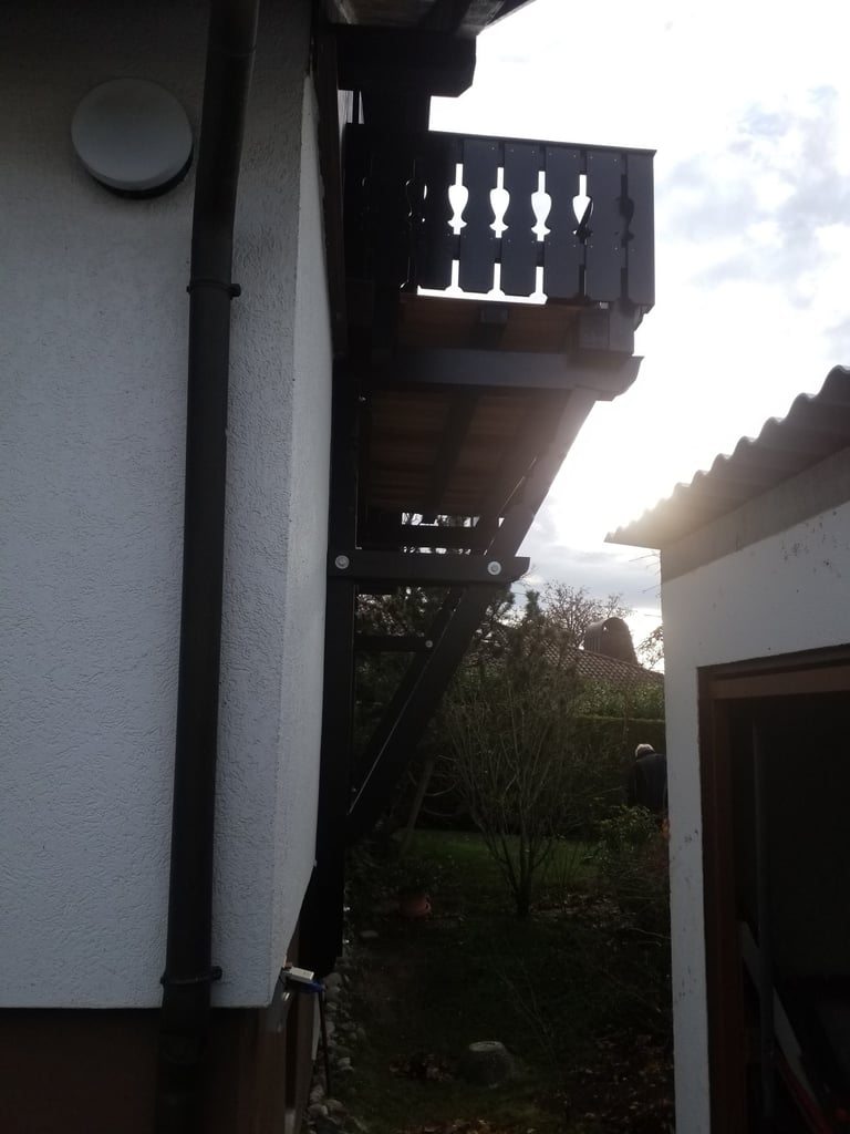 Seitliche Ansicht eines Hauses mit Balkon und Stahlstützen im schmalen Zwischenraum zur Nachbargarage.