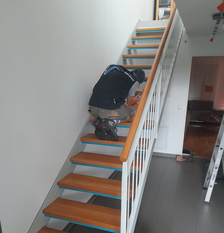 Handwerker kniet auf einer Holztreppe und montiert/arbeitet an den Stufen im Innenbereich.