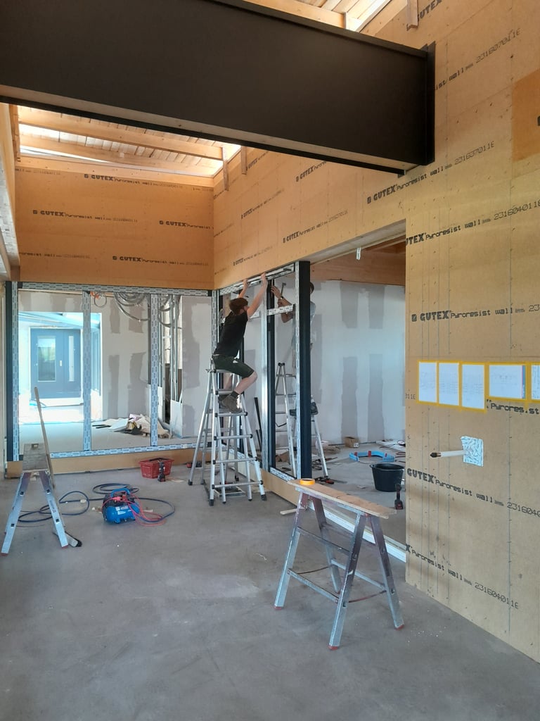 Montage einer großen Schiebe-Glasfront im Neubau, Schreiner arbeitet auf Leiter in Rohbau-Interior