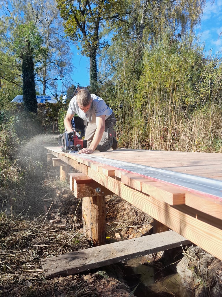 Schreiner sägt im Freien Holzbohlen für einen Steg mit einer Kreissäge zu.