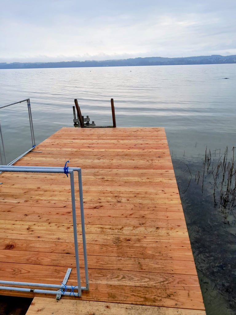  Holzsteg ragt in einen ruhigen See mit Blick auf das gegenüberliegende Ufer vom Ammersee.
