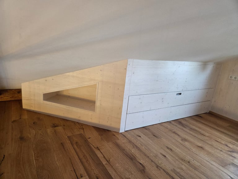 Maßgefertigter Einbauschrank aus hellem Holz unter der Dachschräge mit offener Nische und Schubladen.
