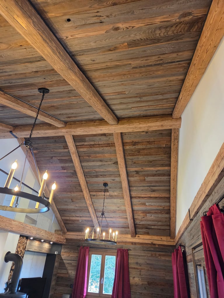 Hoher Sichtdachstuhl aus rustikalem Altholz mit massiven Balken und zwei schwarzen Kronleuchtern.
