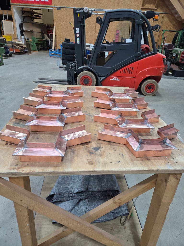 Handgefertigte Kupfer-Abdeckungen und Kantteile auf Werkbank in der Werkstatt, im Hintergrund Gabelstapler.